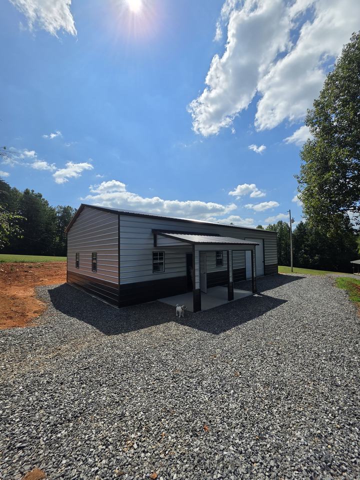 Finished metal garage with a covered front porch, walk-in door and windows on a gravel drive